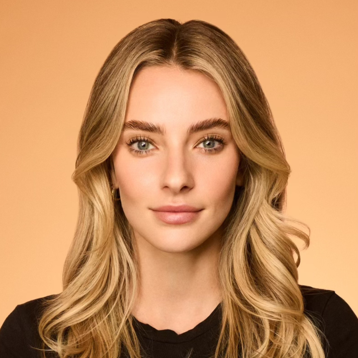 Woman with blonde wavy hair and natural makeup against a warm peach background